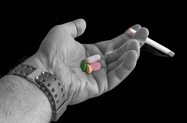 Lighted cigarette in hand with medicinal pills on the palm isolated in dark background