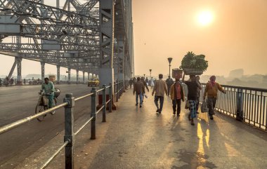 Satıcılar ve commuters Howrah bridge onların günlük faaliyetleri için bir soğuk puslu kış sabahı Hooghly Nehri üzerinde çapraz.