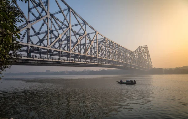 Puente histórico Howrah en el río Hooghly en una mañana brumosa de invierno con un barco de pesca pasando el puente . — Foto de Stock