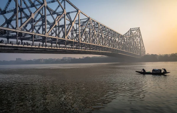 Puente histórico Howrah en el río Ganga en una mañana de invierno brumosa con un barco pesquero de madera pasando el puente . — Foto de Stock