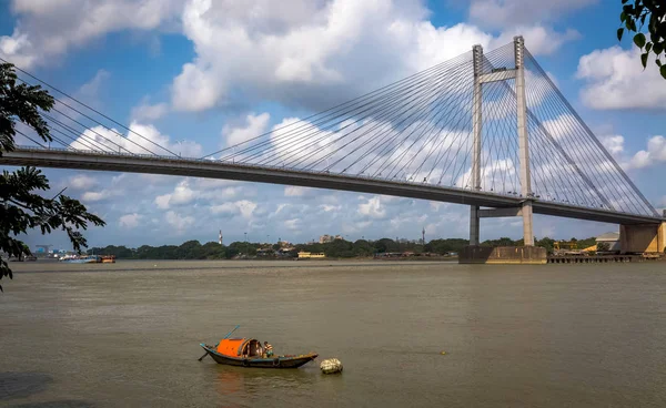 Holzboot auf dem Fluss Hooghly mit der Vidyasagar Setu-Brücke als Hintergrund. die längste seilbrücke Indiens, die die stadt kolkata mit dem bezirk howrah verbindet. — Stockfoto