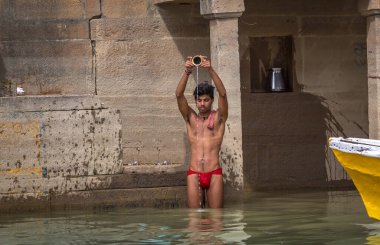 Varanasi, Hindistan, 13 Ekim 2017: Genç adam, Hindistan 'ın Varanasi kentindeki Ganj nehri ghatındaki sabah namazı ritüeli kapsamında Ganj Nehri' ne su sunuyor..