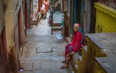 Varanasi, Hindistan, 12 Ekim 2017: Varanasi şehir geçidi eski yıpranmış binalar ve kapısında oturan yaşlı bir kadın. 