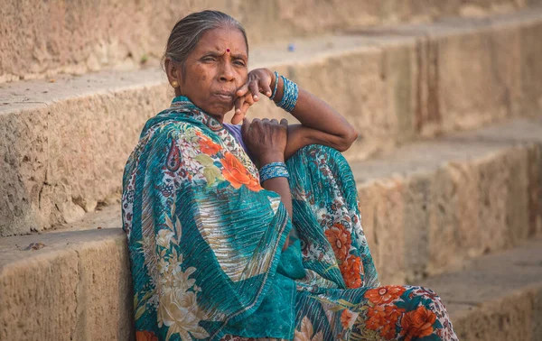 Varanasi, India, October 14,2017: Indian aged woman with a thoughtful expression sitting on the stairways of the Ganges river ghat at Varanasi, India.