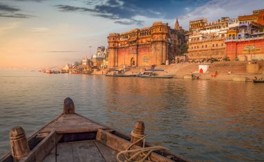 Varanasi Ganges nehir ghat ile antik mimari binalar ve tapınaklar gün batımında nehir üzerinde bir tekne görüntüsü.