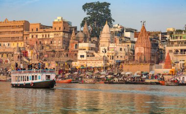 Varanasi, Hindistan, 12 Ekim 2017: Turistler, Hindistan 'ın Varanasi kentindeki antik mimari binalar ve tapınaklar manzaralı Ganj Nehri üzerinde tekne turunun keyfini çıkarıyorlar.