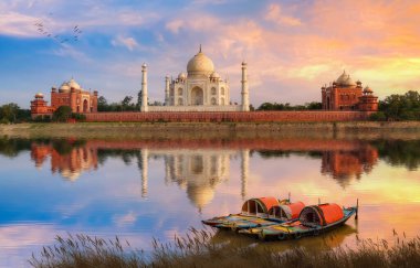 Taj Mahal Agra, gün batımında Yamuna nehrinin kıyısında kasvetli bir gökyüzü ve nehirde turist gezintisi için kullanılan ahşap tekneleri görüyor. 