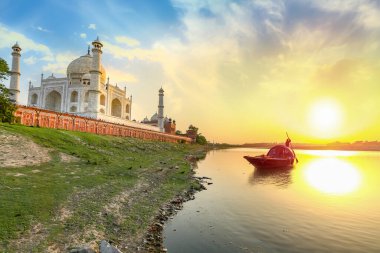 Taj Mahal ortaçağ beyaz mermer mozolesi günbatımında Yamuna nehrinin kıyısında ahşap kayıkla