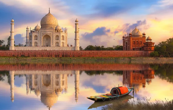 Taj Mahal Agra gün batımında Yamuna nehrinin kıyısında kasvetli günbatımı gökyüzü ve nehirde turist gezisi için kullanılan ahşap tekne manzarası. 