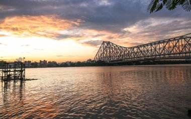 Tarihsel Howrah Köprüsü - Hooghly nehrinin üzerinde kasvetli günbatımı gökyüzü olan bir köprü