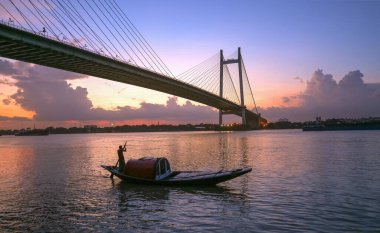 Alacakaranlıkta Ganj nehrinde inşa edilen Vidyasagar Setu olarak bilinen Kolkata Hindistan 'da ahşap bir kayık manzaralı bir köprü olarak kaldı.
