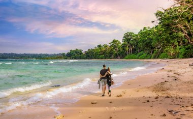 Sahne Neil Adası Andaman Hindistan kıyısı gün batımında genç turist çiftle kumsalda yürüyüş yapıyor.