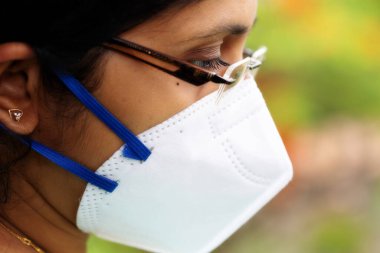 Korona virüsü salgınına karşı önlem olarak yakın planda N95 maskesi takan Hintli kadın.