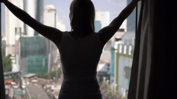 Silueta ženy odhalení záclony a při pohledu z okna. Město mrakodrapů krajina mimo