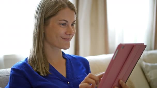 Žena sedí na pohovce s tabletu. Prohlížení internetu s úsměvem, komunikaci se svými přáteli