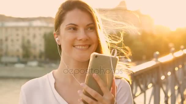 Boldog, fiatal nő, pihentető a szabadban. Gyönyörű lány hallgat zenét a smartphone. Nyári nap süt