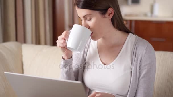 S úsměvem profesionální žena pracující na přenosném počítači v domácí pití kávy. Koncepce domácí kanceláře