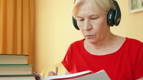 Starší žena v bezdrátových sluchátek trénink poslechu znalosti cizích jazyků, psaní v učebnici