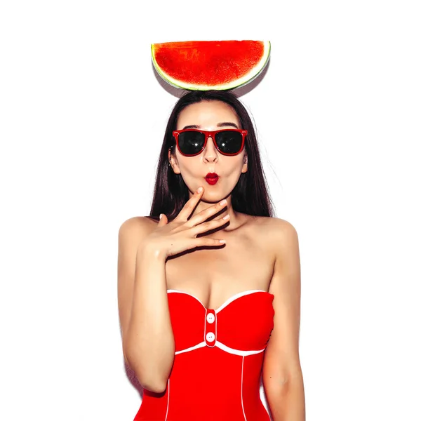 Сексуальна мода здивована жінка з кавуном на її голові в бікіні з червоними губами та сонцезахисними окулярами на білому ізольованому фоні. Портрет стилю спалаху крупним планом . — стокове фото