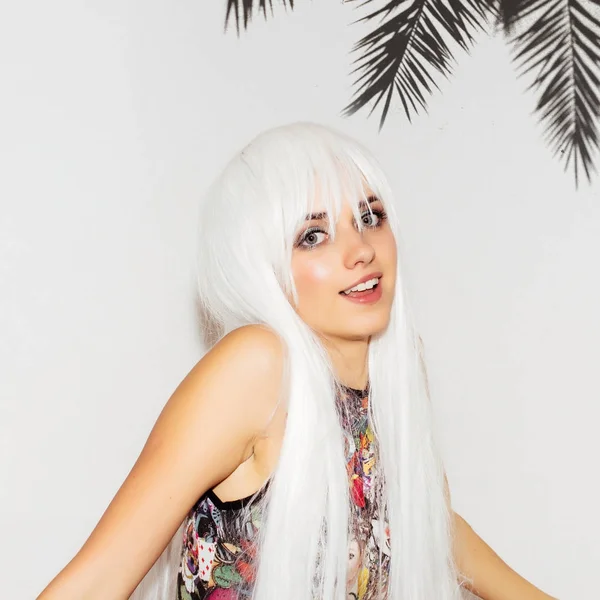 Szép nyári nő mutatva fogát palm tree háttérrel. Vidám vicces játékos aranyos kislány a színes ruhák és fehér paróka mutat hogyan tökéletes fogakkal mosolyogni. Szórakoztató csípő lány. — Stock Fotó