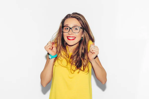 Renkli stüdyo portre, Hipster gülümseyen kız moda eller kalçalara beyaz arka plan ile. Eğlenceli olumlu genç akıllı kadın gözlük ve mükemmel ile gülümseyen renkli sarı tişört.