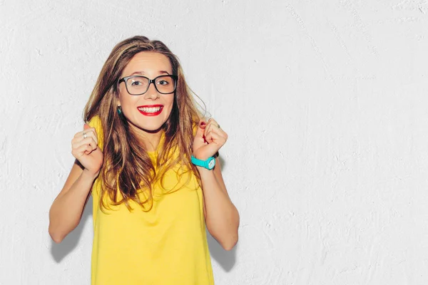 Renkli stüdyo portre, Hipster gülümseyen kız moda eller kalçalara beyaz arka plan ile. Eğlenceli olumlu genç akıllı kadın gözlük ve mükemmel ile gülümseyen renkli sarı tişört.