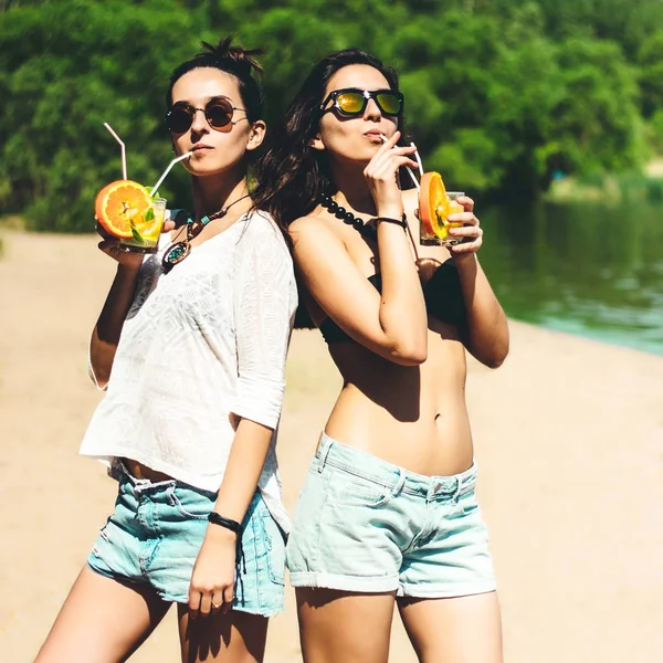 Duas meninas atraentes gêmeos hipster com coquetéis na praia desfrutando de férias em uma ilha tropical, corpo bronzeado perfeito, pele saudável, sexy elegante casual wear, biquíni, gêmeos morena em óculos de sol — Fotografia de Stock