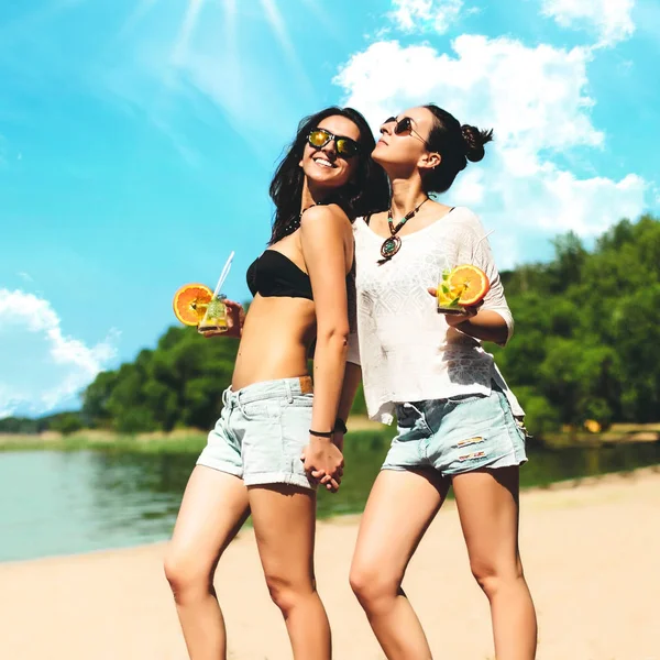 Duas meninas gêmeas hipster na moda legal com coquetéis na praia desfrutando de férias em uma ilha tropical, corpo bronzeado perfeito, pele saudável, desgaste casual sexy elegante, biquíni, gêmeos morena em óculos de sol — Fotografia de Stock