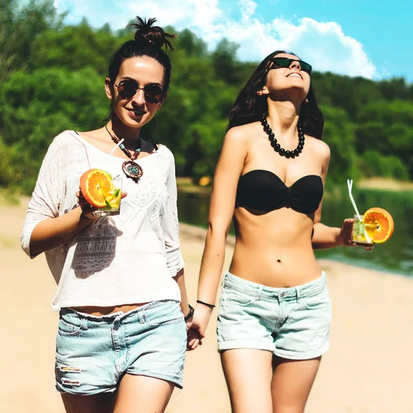 Δύο δίδυμα κορίτσια δροσερό trendy hipster με κοκτέιλ στην παραλία απολαμβάνουν διακοπές σε ένα τροπικό νησί, τέλεια μαυρισμένο σώμα υγιές δέρμα, σέξι και κομψό καθημερινό ντύσιμο, μπικίνι, Μελαχρινή δίδυμα σε γυαλιά ηλίου — Φωτογραφία Αρχείου