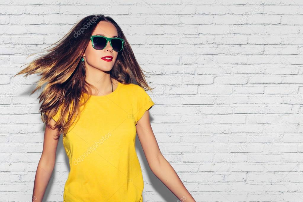 Colorful Studio Portrait of Hipster Fashion Smiling Girl with Hands on Hips at white Background. Fun positive young smart woman in glasses and colorful yellow shirt smiling with perfect teeth.