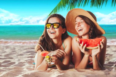Tatil. Yaz seyahat. İki kız genç kadınlar bikinili kokteyller ve karpuz palmiye ve gökyüzü arka plan ile kum üzerinde döşeme kamera gülümseyen güneş gözlüğü ile tropik Sahilde güneşlenmek