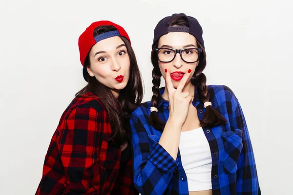 Fun girl stick tongue out between two fingers showing cunnilingus sign. Colorful comic funny emotional hipster summer style twins teenager girls make faces and have fun. Isolated on a grey background.