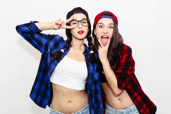 Fun girl stick tongue out between two fingers showing cunnilingus sign. Colorful comic funny emotional hipster summer style twins teenager girls make faces and have fun. Isolated on a grey background.