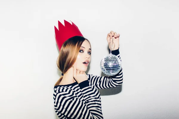 Young smiling woman celebrating party, wearing stripped dress and red paper crown, happy dynamic carnival disco ball party, excited, having fun, smiling, laugh. White background — Stock Photo, Image