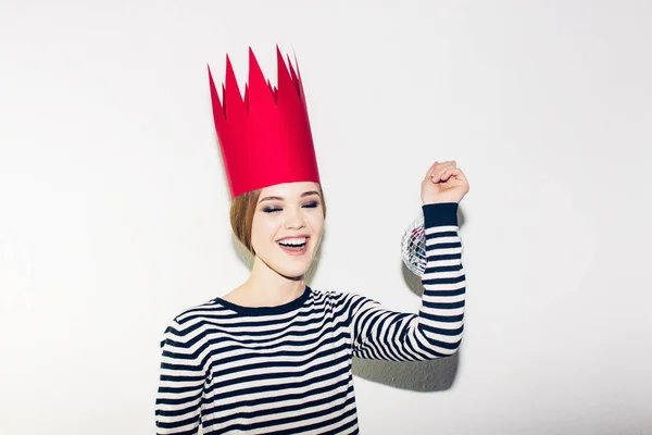 Jeune femme souriante célébrant la fête, portant une robe dénudée et une couronne en papier rouge, joyeuse fête dynamique de carnaval disco ball, excitée, s'amusant, souriante, rire. Fond blanc — Photo