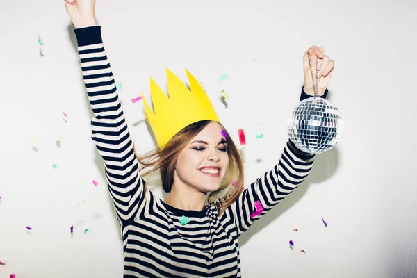 Jeune femme souriante sur fond blanc fête, portant une robe dénudée et une couronne en papier jaune, joyeuse fête dynamique de carnaval, confettis étincelants, s'amuser, sourire, rire . — Photo