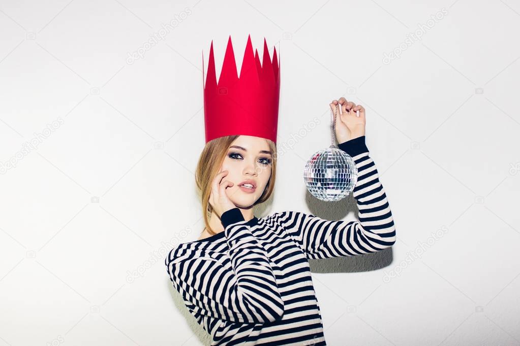 Young smiling woman celebrating party, wearing stripped dress and red paper crown, happy dynamic carnival disco ball party, excited, having fun, smiling, laugh. White background