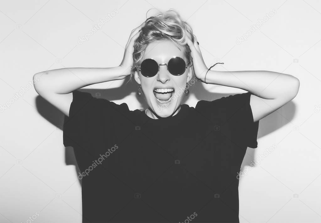 Stylish fashion sexy blonde bad crazy girl in a black t-shirt and rock sunglasses scream holding her head. Dangerous rocky emotional woman. white toned. background, not isolated