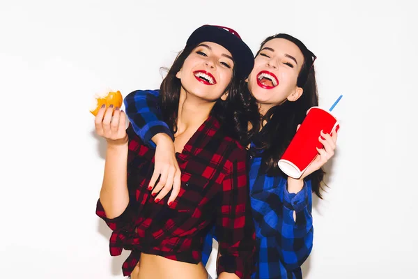 Jovens hipster meninas se divertindo bebendo um refrigerante de palha e segurando um hambúrguer, sorriso feliz e rir no fundo branco . — Fotografia de Stock