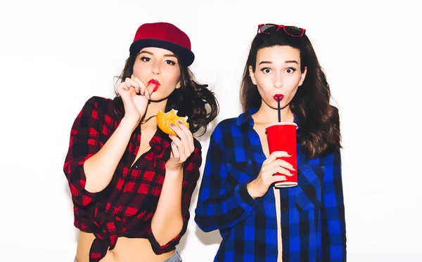Jóvenes chicas hipster divirtiéndose bebiendo un refresco de paja y sosteniendo una hamburguesa, sonrisa feliz y risa en el fondo blanco . —  Fotos de Stock