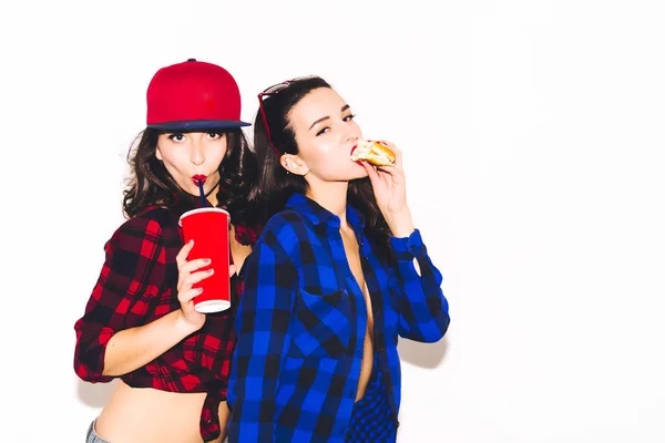 Fiatal hipster lányok szórakozás ivott egy kólát a szalma és a gazdaság egy hamburgert, boldog, mosolyog, és nevetni a fehér háttér. Stock Kép