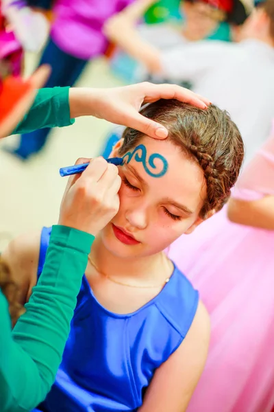 The child draw the face on the children's holiday. Aqua make-up