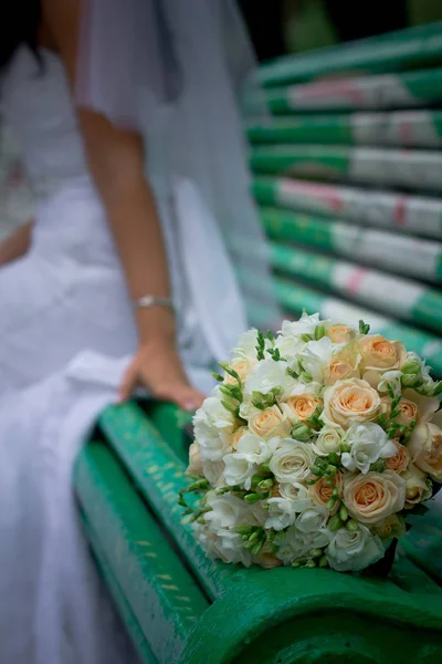 The brides bouquet lies on a green bench