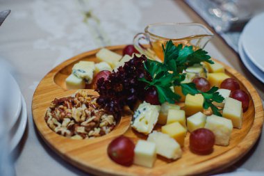 Bir ziyafette restoranda peynir tabağı. Aperatifli masa ayarları. Dilimlenmiş peynirli ahşap tepsi