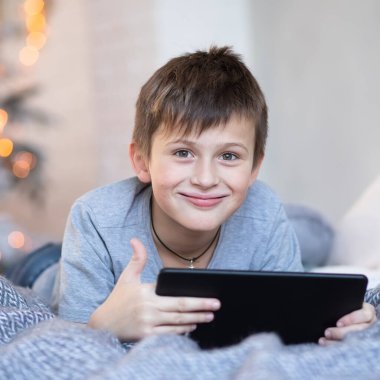 Elinde tablet olan mutlu yakışıklı çocuk. Çocuk tablette bilgisayar oyunları oynuyor. Erkek çocuk Noel 'den önce Noel ağacının karşısında yatar. Kara Cuma ve Siber Pazartesi İnternetten Alışveriş