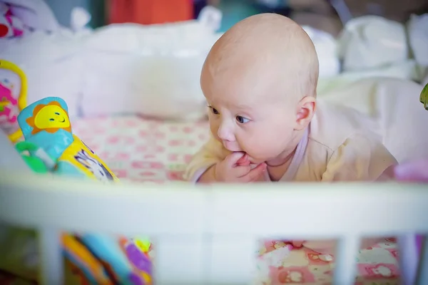 Pequeno bebê recém-nascido encontra-se no berço e olha para o desenvolvimento do livro. Desenvolvimento precoce de crianças . — Fotografia de Stock