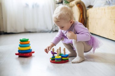 Montessori tahta oyuncağı katlanmış piramit. Kız güneşli bir günde oturma odasında yerde mantıksal piramit oynuyor. Çember, dörtgen, üçgen, çocuk oyuncaklarının tahta unsurlarını dikdörtgen yap. oyuncak mavi, sarı, kırmızı