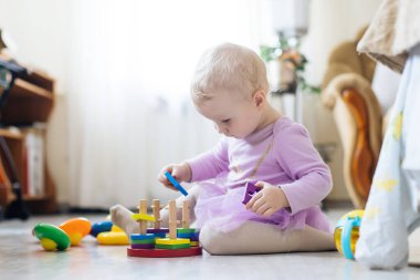 Kız oturma odasında oyuncak oynuyor. Montessori tahta oyuncağı katlanmış piramit. Çember, dörtgen, üçgen, çocuk oyuncaklarının tahta unsurlarını dikdörtgen yap. Çok renkli oyuncak mavi, sarı, kırmızı, yeşil.