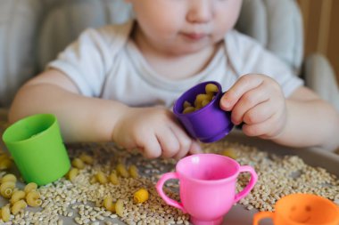 Çocuk buğday tanelerinden kuru makarna seçiyor. Ürünleri sıralıyorum. Çocuklarla mantıklı oyunlar. Çocukların bir yıla kadar erken gelişim kavramı.