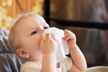 Çocuk burnunu beyaz mendille siler. Hasta çocuk beslenme sandalyesinde oturarak yemek yiyor. Soğuk rhinitis 'li bir çocuk. Virüs ve enfeksiyon. Coronavirus belirtileri. yan görünüm